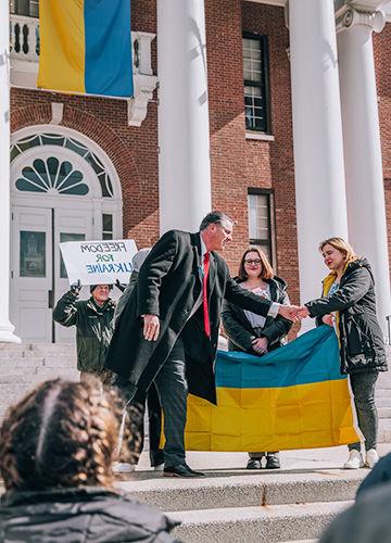 BSU 总统 Fred Clark shaking h和s with students holding the Ukrainian flag in front of Boyden Hall; a man holds a sign that says Freedom for Ukraine